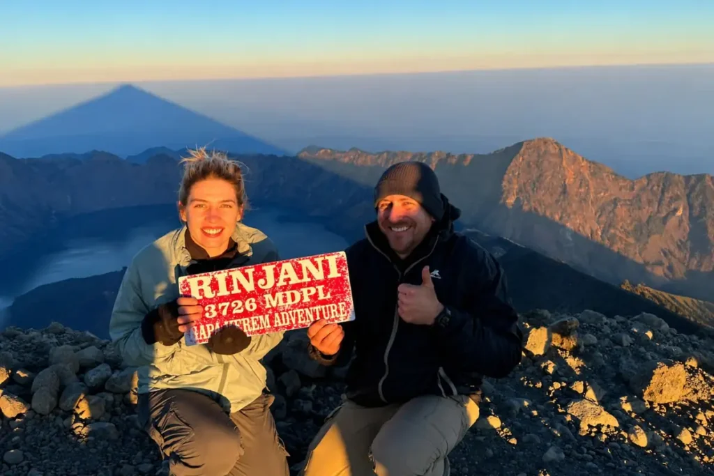 Hikers reaching the summit of Mount Rinjani during a 4-day 3-night trekking adventure with panoramic views of the crater lake and surrounding mountains.